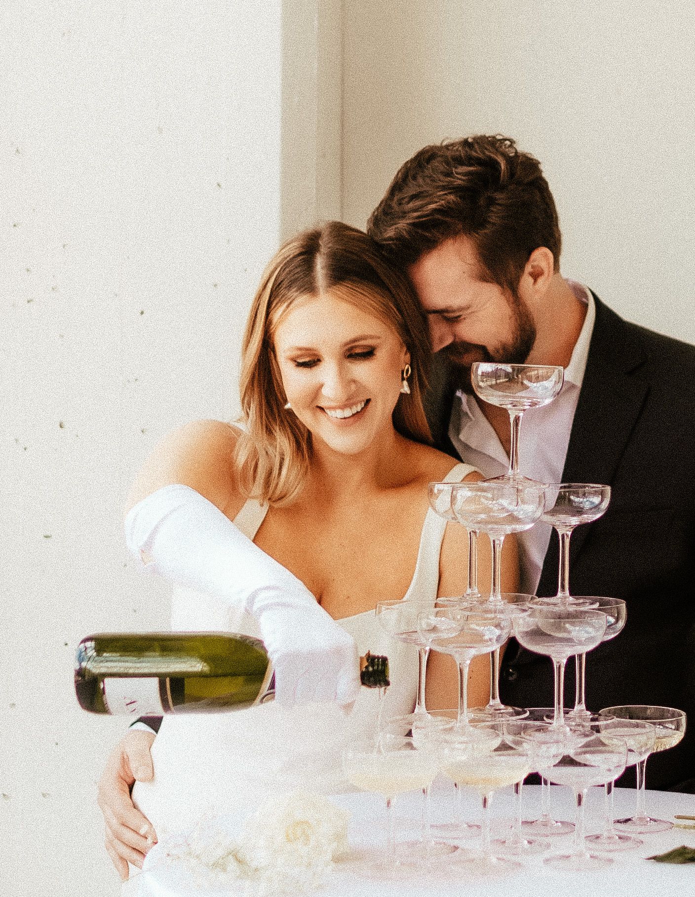 Couple pours champagne into tower of vintage coupe glasses.