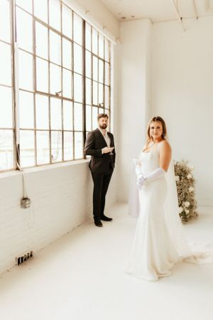 Elegant wedding portrait in a bright industrial loft space with tall windows and white walls.