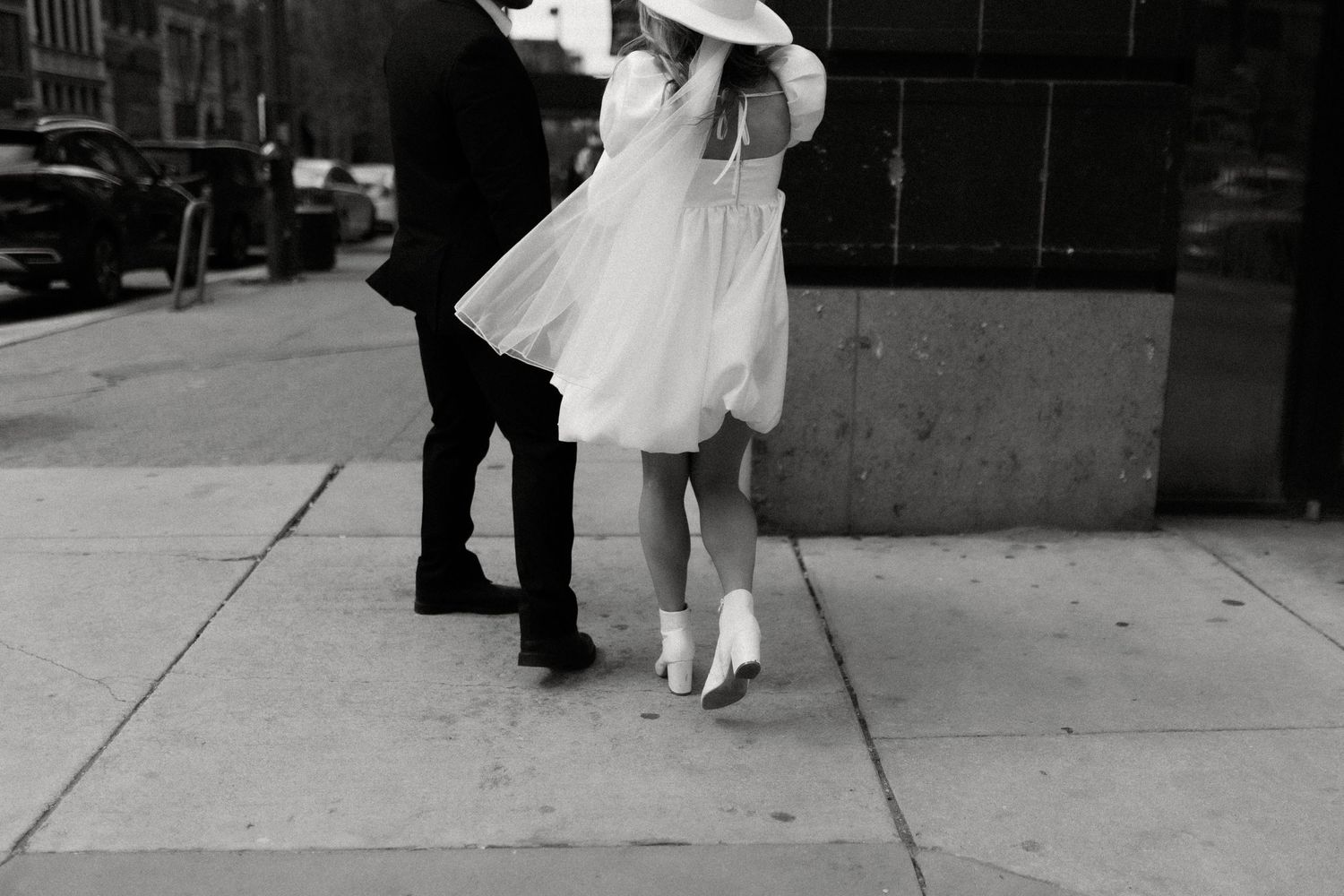 Black and white photo of a couple's feet in formal attire dancing on a city sidewalk.