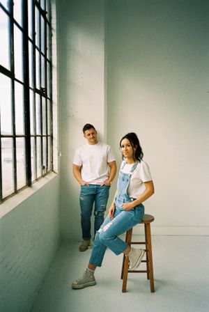 Casual couple in denim and white t-shirts poses by industrial window.