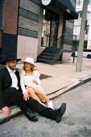 Couple in vintage clothing sits casually on city sidewalk steps.