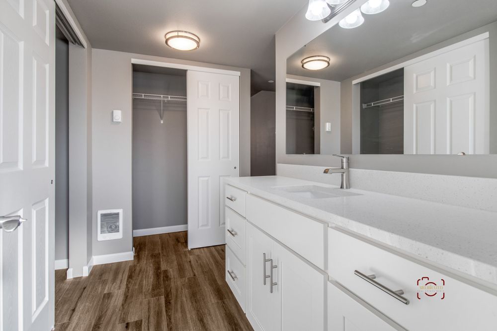 White bathroom with double vanity, hardwood floors, and built-in closet storage.
