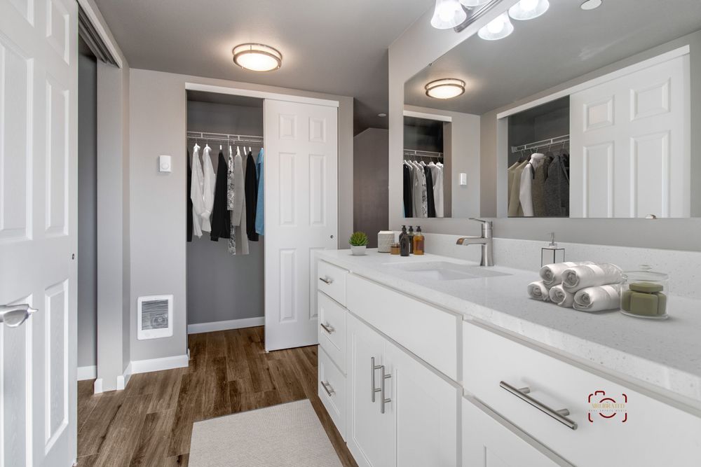 Modern bathroom featuring double sinks, white cabinetry, and walk-in closet space.