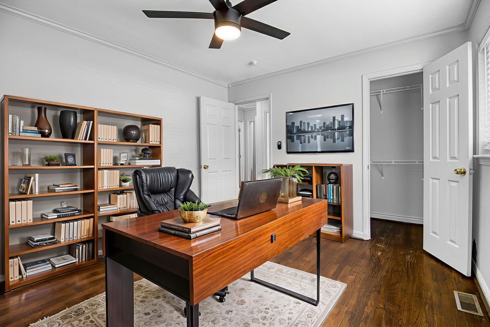 Modern home office with wooden floors, ceiling fan, built-in shelving, and an orange accent wall showcasing professional decor.