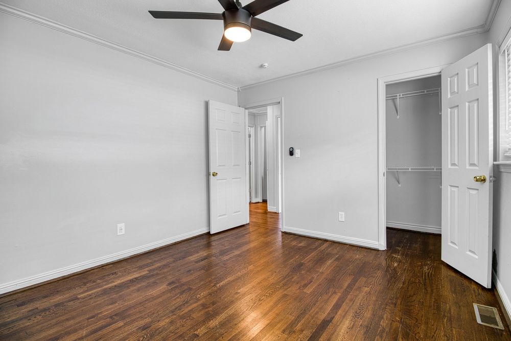 Empty bedroom with hardwood floors, white walls, and a ceiling fan shows two doorways.