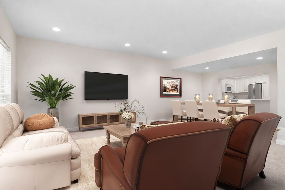 Modern living room with leather chairs, wall-mounted TV, open kitchen, and neutral tones in a bright, spacious layout.