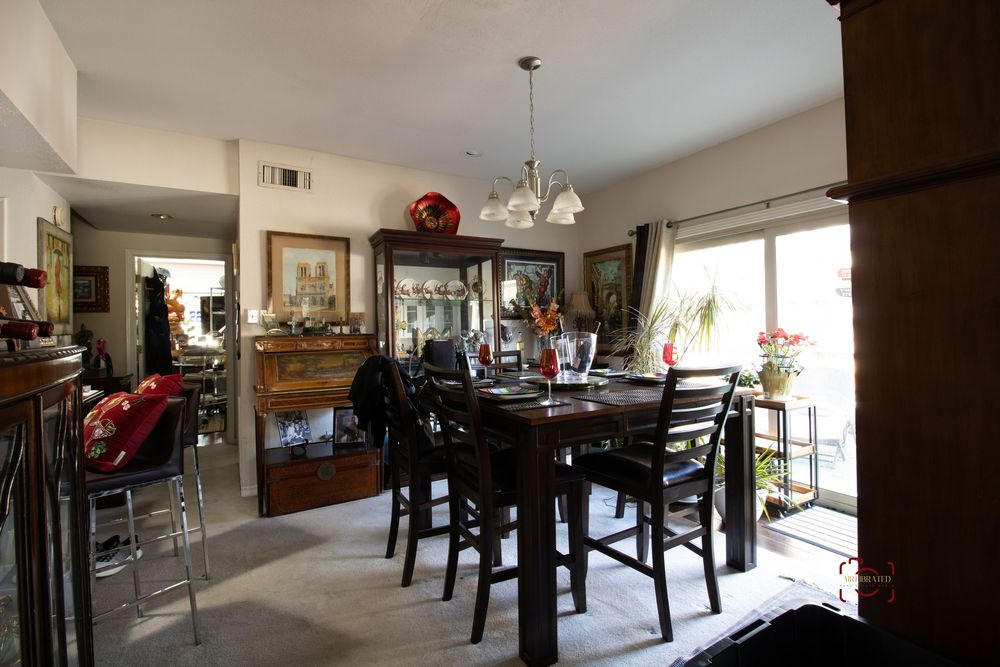 Elegant dining room with dark wood table, chairs, chandelier, hutch, and natural light from large windows.