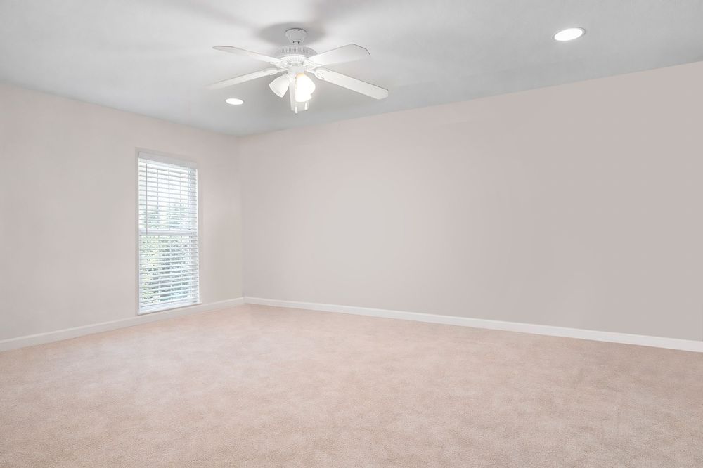 Spacious empty bedroom with light beige carpet, white ceiling fan, recessed lighting, and a window with blinds.