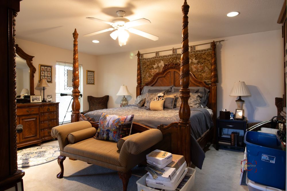Elegant master bedroom featuring a grand four-poster bed, ornate wooden furniture, ceiling fan, and neutral carpet flooring.