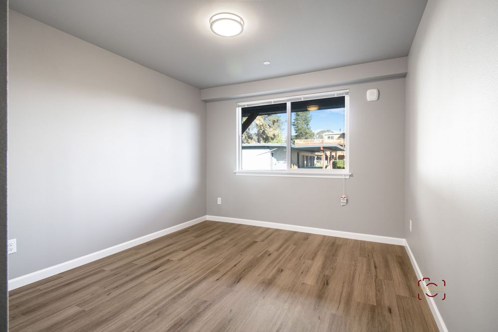 Empty bedroom with hardwood floors, window, and modern ceiling light fixture.