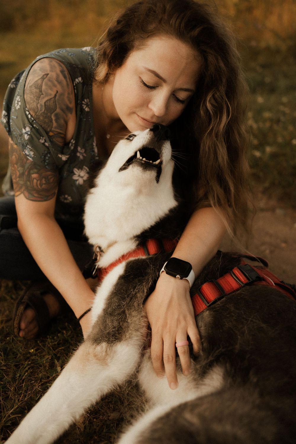 A Husky dog wearing a red harness shares an affectionate moment on a nature trail.