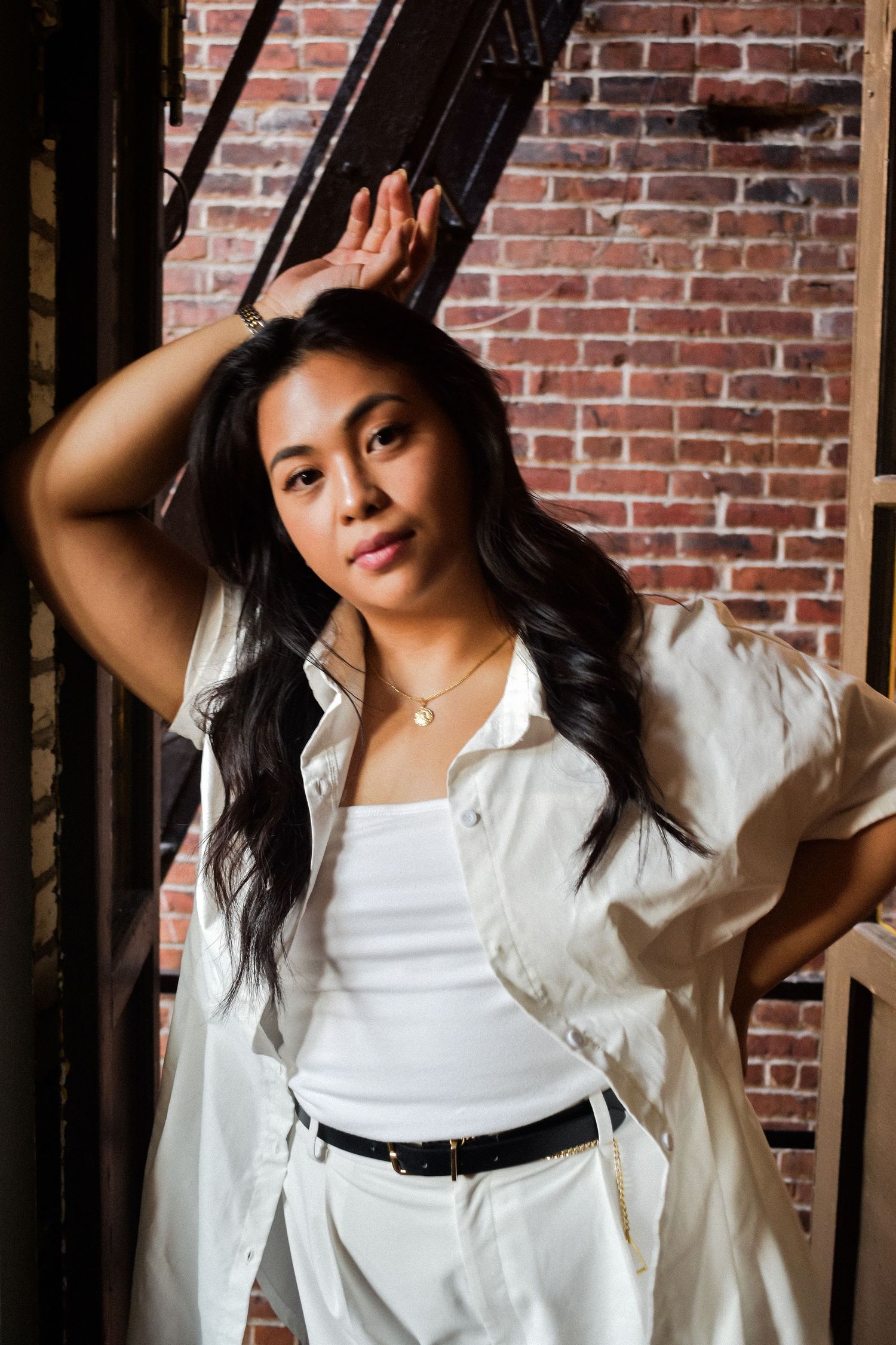 Stylish portrait against brick wall features flowing dark hair, white outfit and casual button-down shirt layered look. Seattle photographer