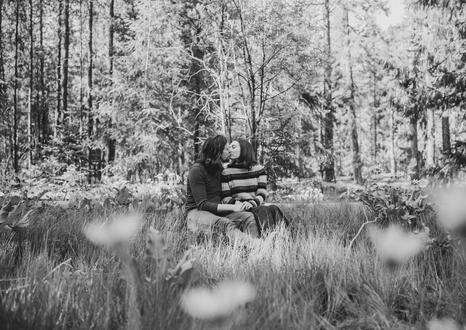 Black and white portrait of a couple sitting together in a meadow with wildflowers.