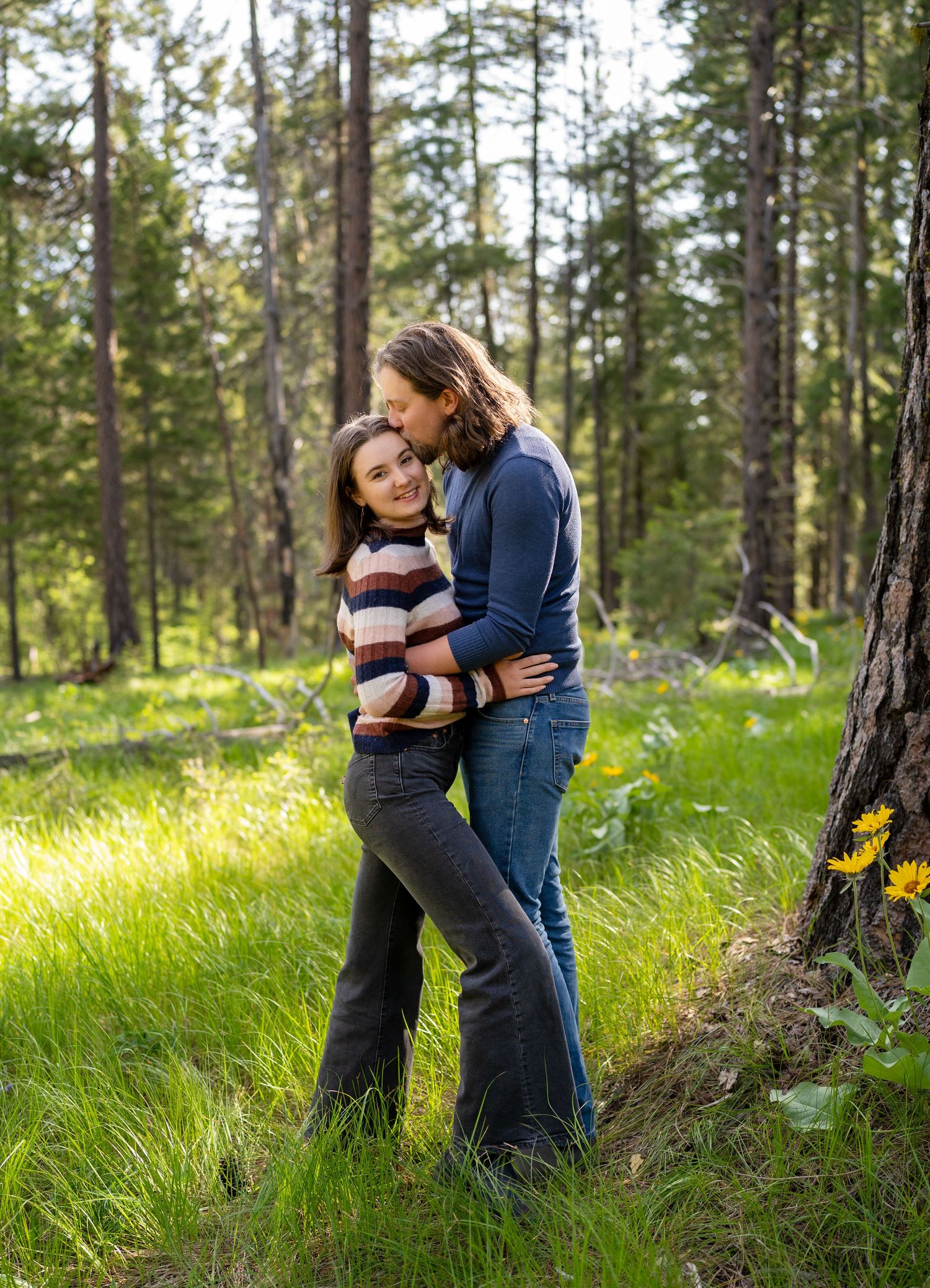A romantic embrace between a couple in a sunlit forest clearing.