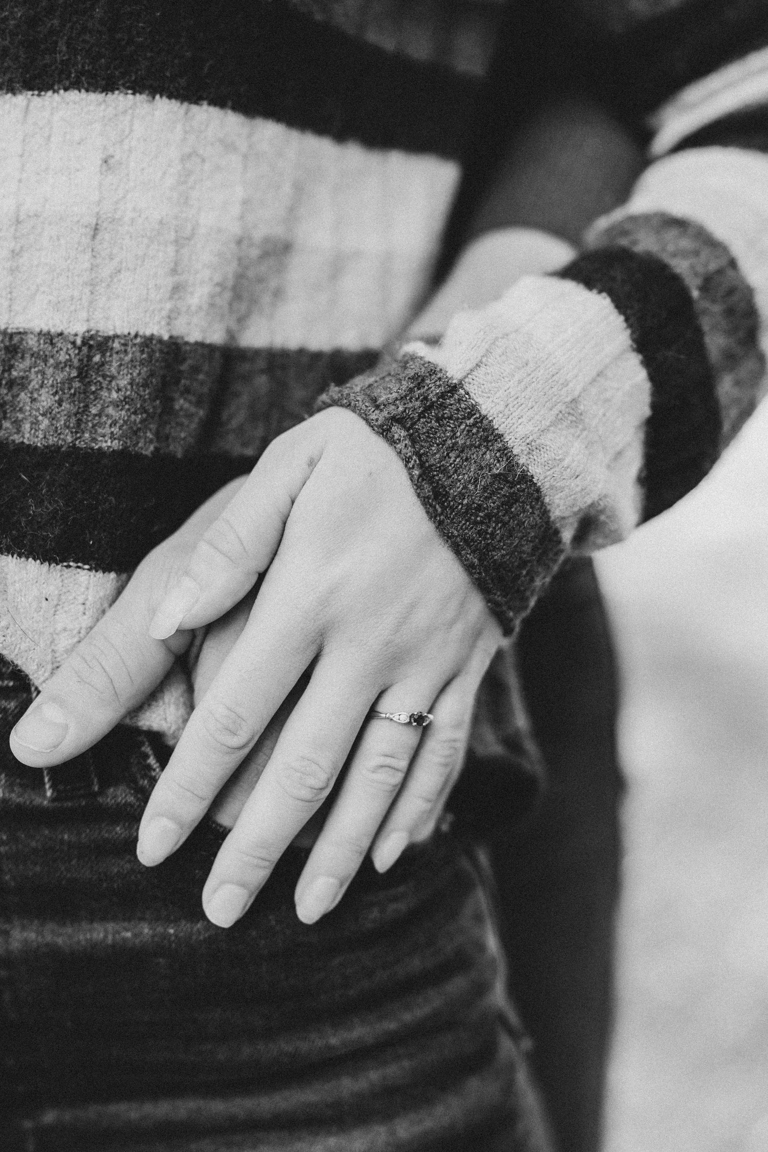 Close-up of a hand wearing a striped sweater sleeve and wedding ring.