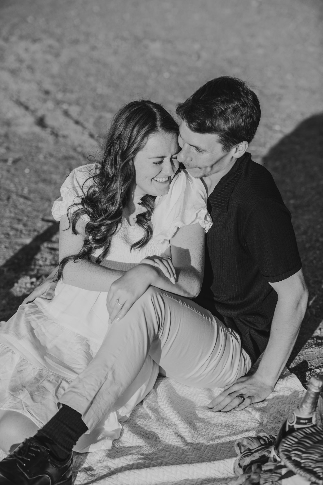 Black and white romantic engagement photo of couple laughing together outdoors.