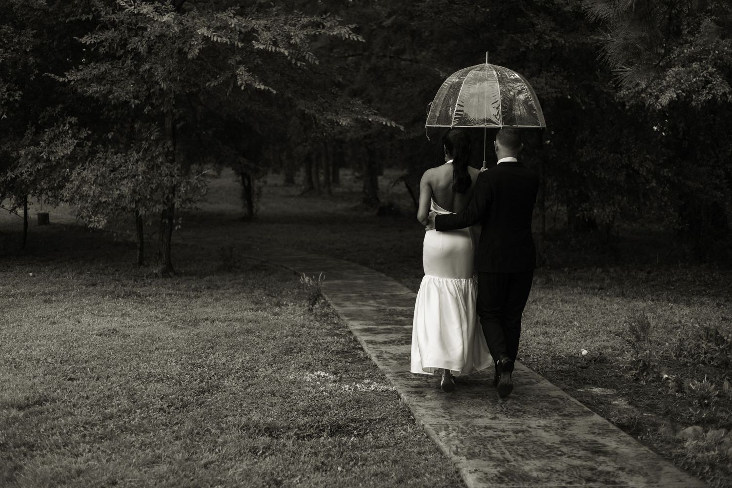 Wedding couple walking on a path through the woods in the rain with an umbrella.