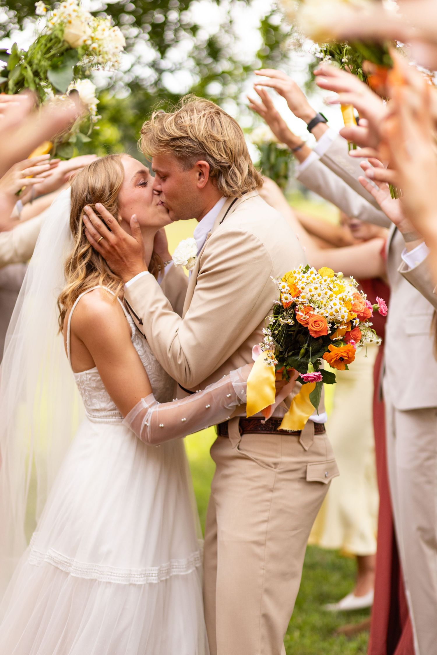 A romantic wedding celebration moment with a bridal bouquet of yellow and orange flowers under a shower of flower petals.