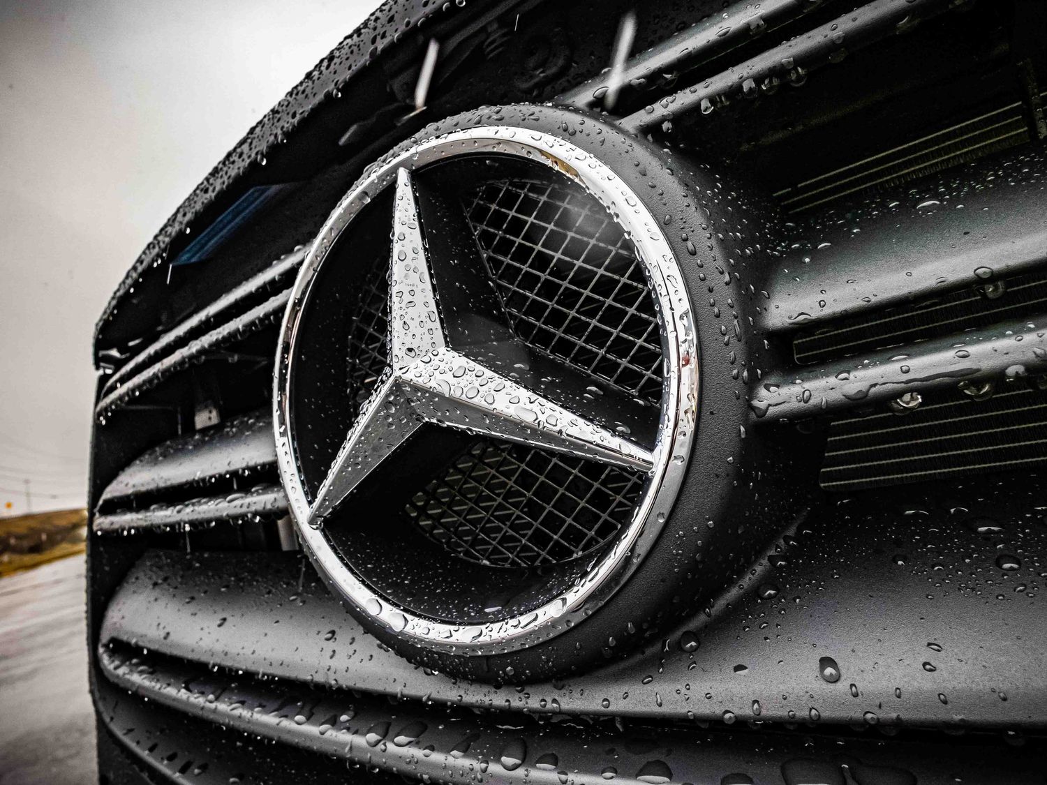 Close-up of a wet Mercedes-Benz logo on a black grille with water droplets.