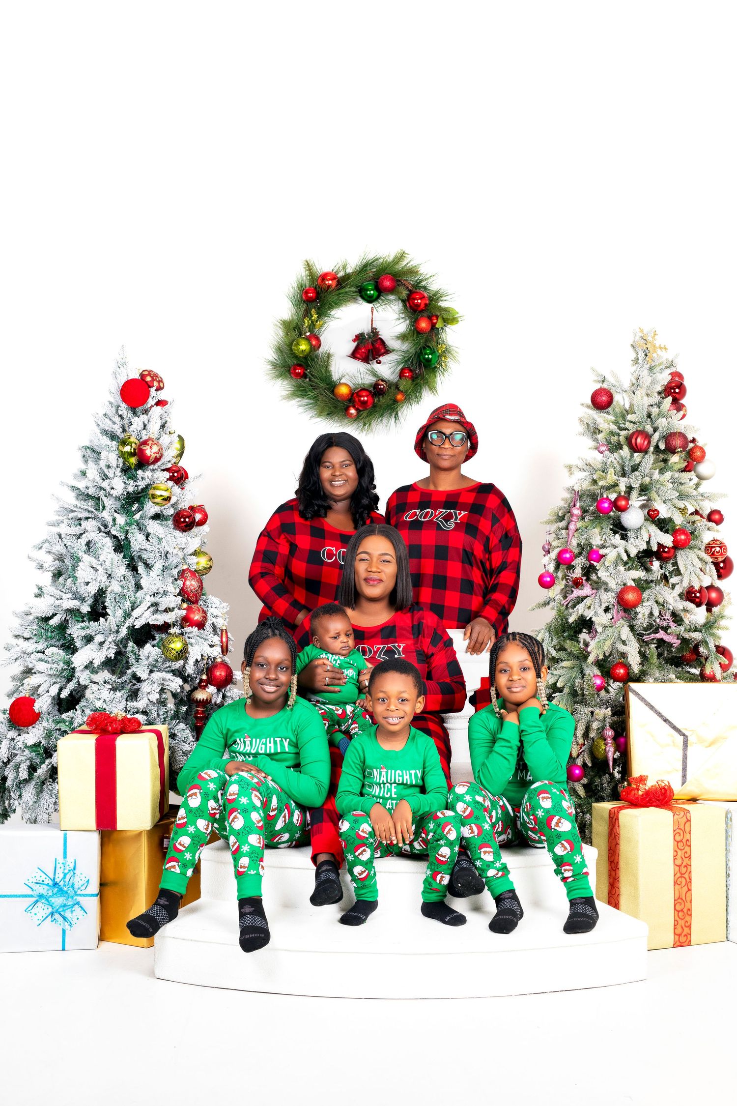 Festive family holiday photo with matching pajamas and decorated Christmas trees.