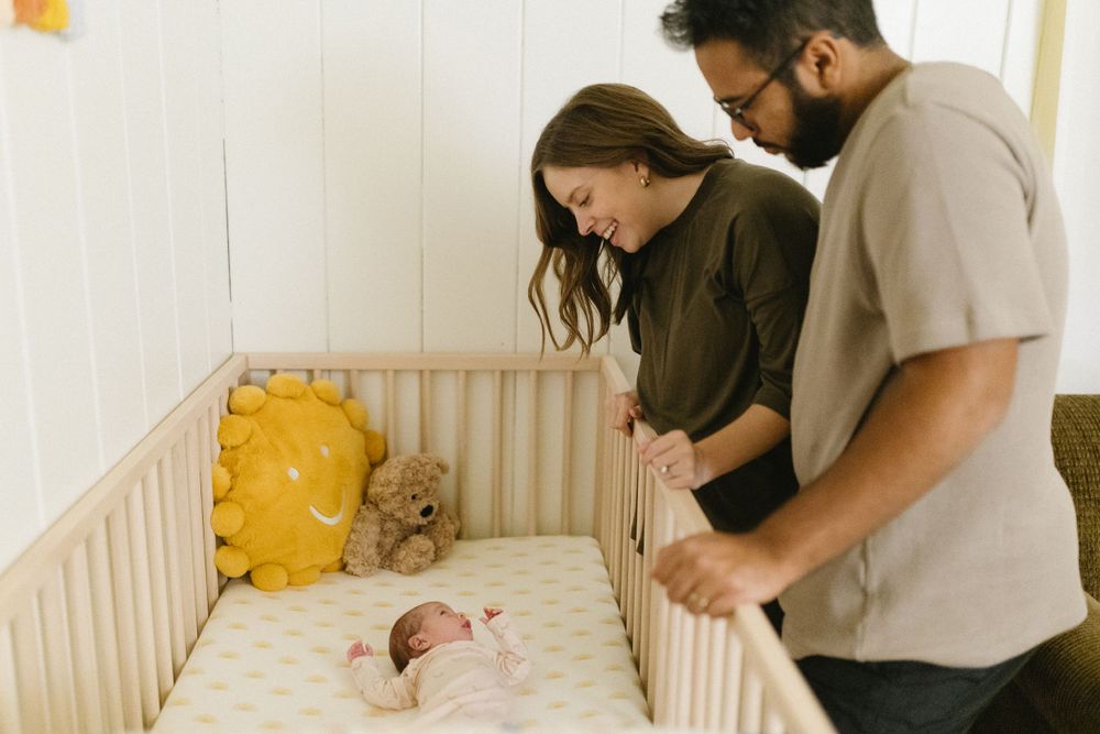 Parents looking down at their newborn baby in wooden crib with yellow accents.