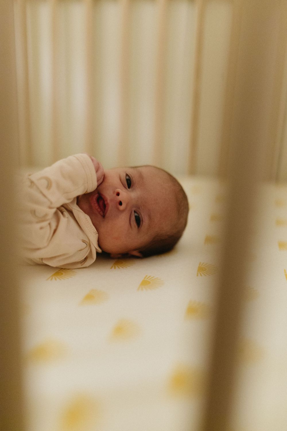 Infant in cream colored onesie lying on polka dot bedding with curious expression.