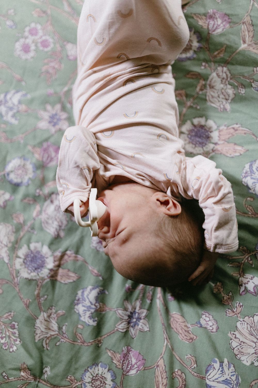 Baby in cream outfit lying on floral bedding during lifestyle photoshoot.