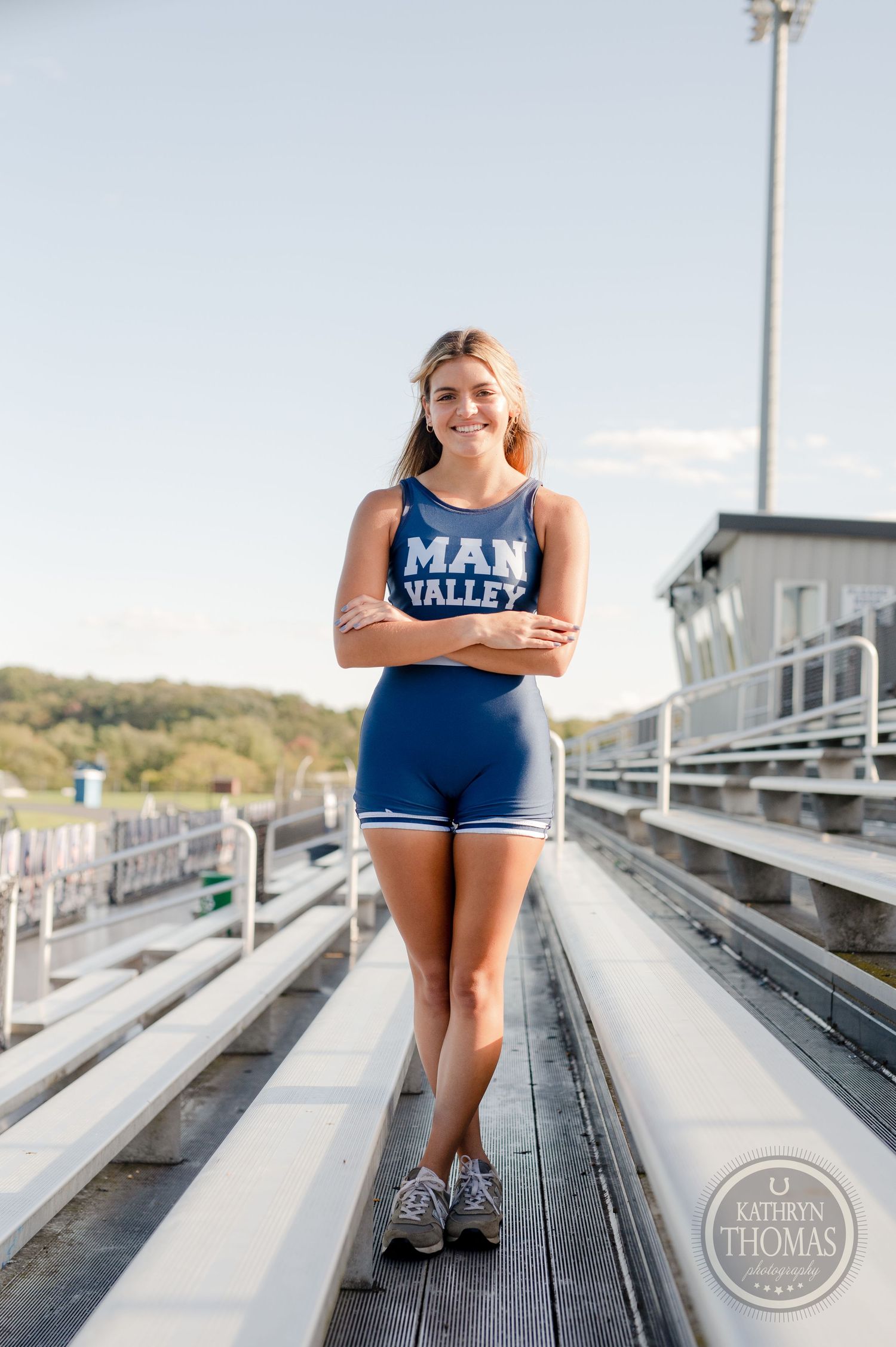 Student athlete stands on stadium bleachers wearing blue Man Valley athletic uniform.