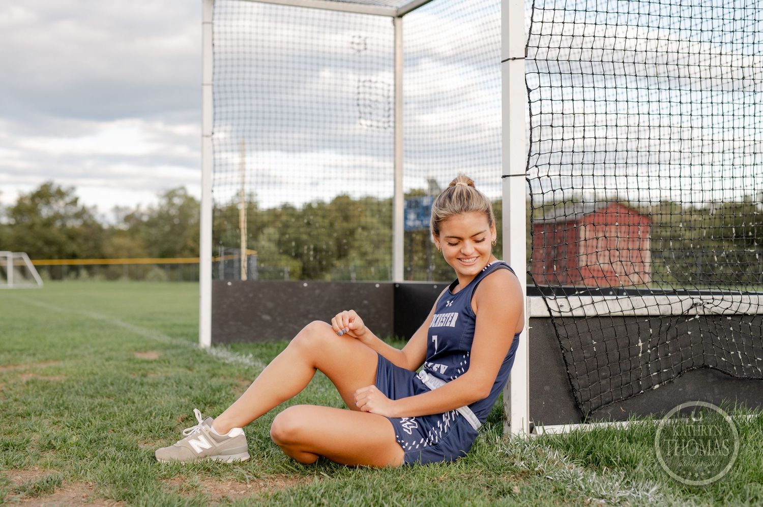 Athlete rests against field hockey goal post on grass field.