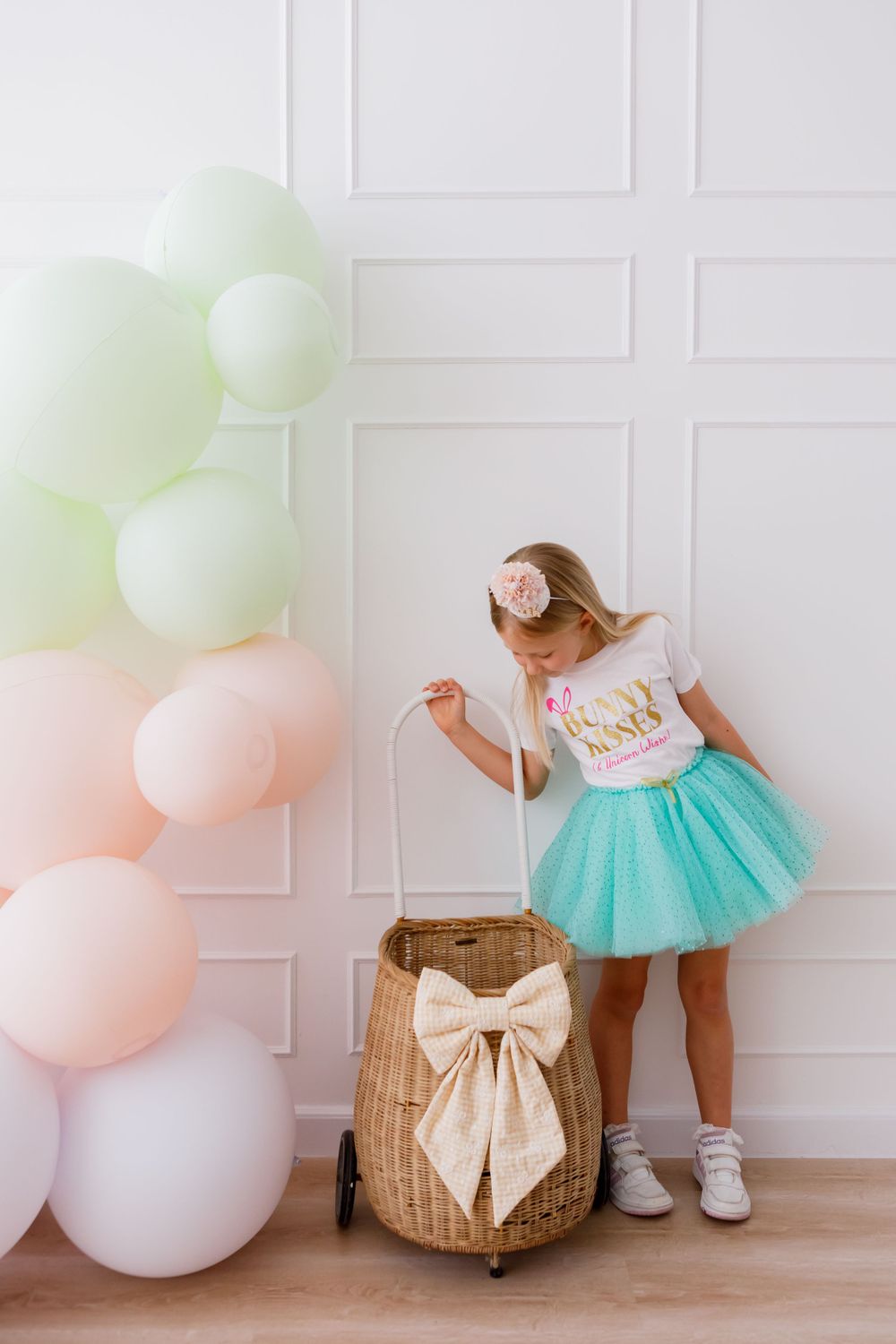 Decorative pastel pink and mint balloon arch next to a wicker basket with large bow and teal tulle skirt.