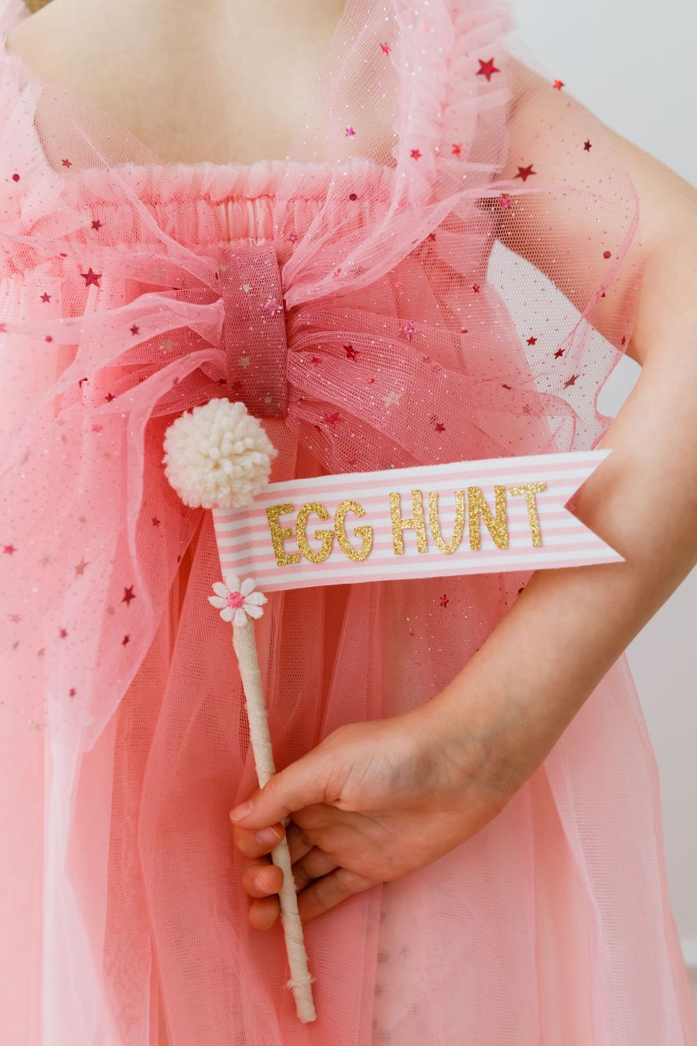 A decorative 'Egg Hunt' sign on a white ribbon with pom pom against pink tulle fabric with glittery star details.