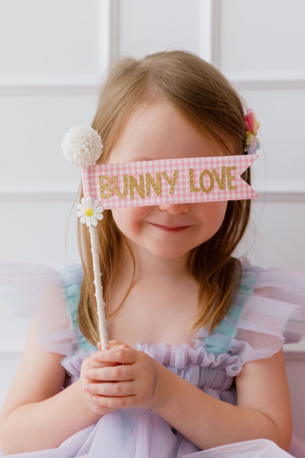 A child in a pastel dress holds a stick with 'Bunny Love' text and floral decorations.