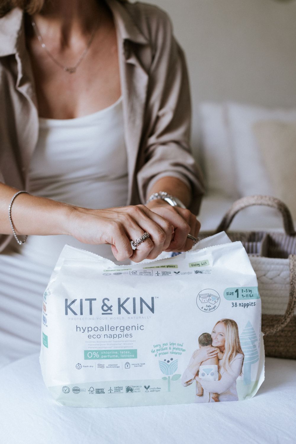 Close-up of hands holding Kit & Kin eco-friendly baby product package on white bedding.