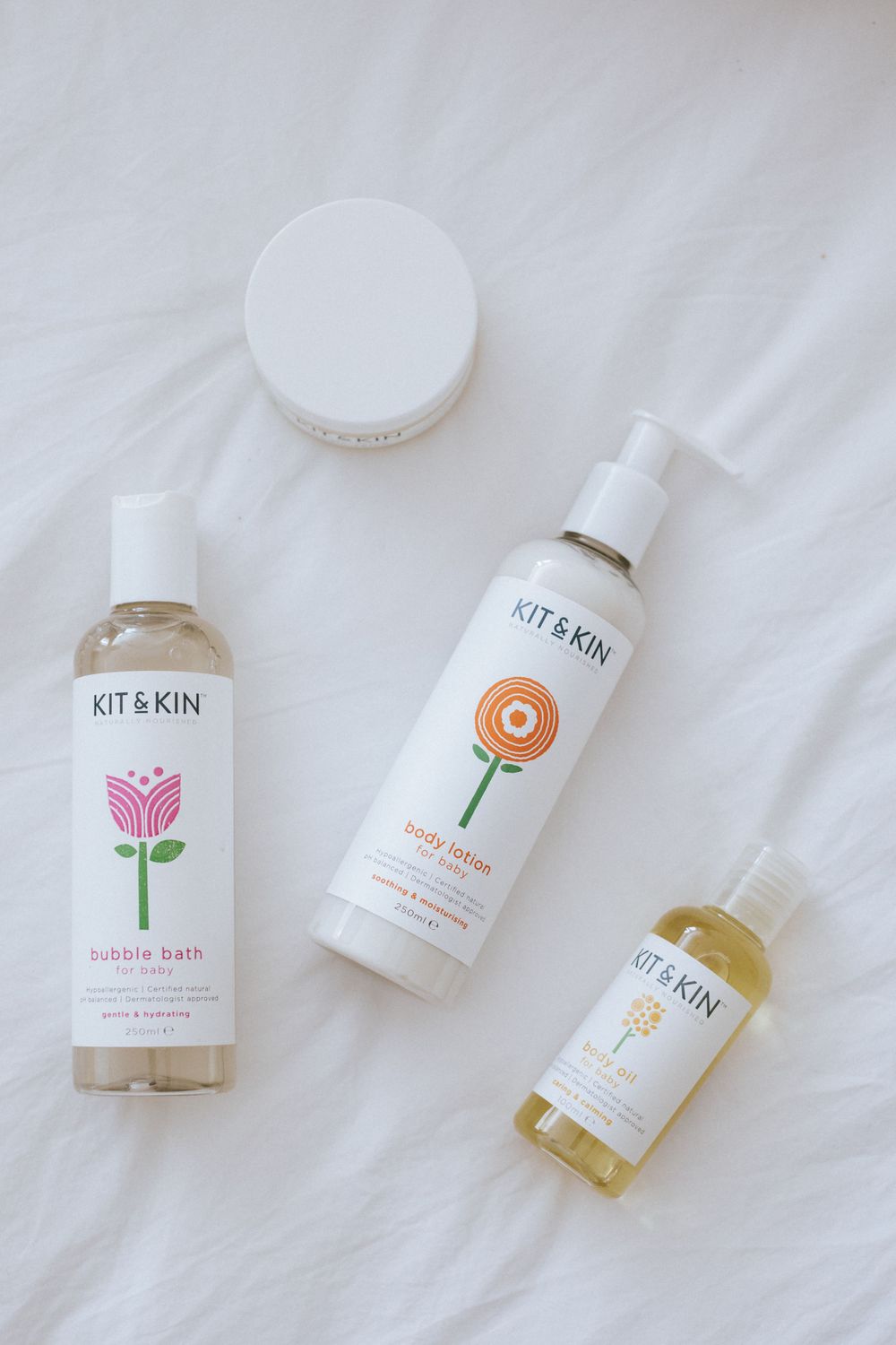 Kit and Kin natural skincare products with floral and botanical designs displayed on white fabric background.