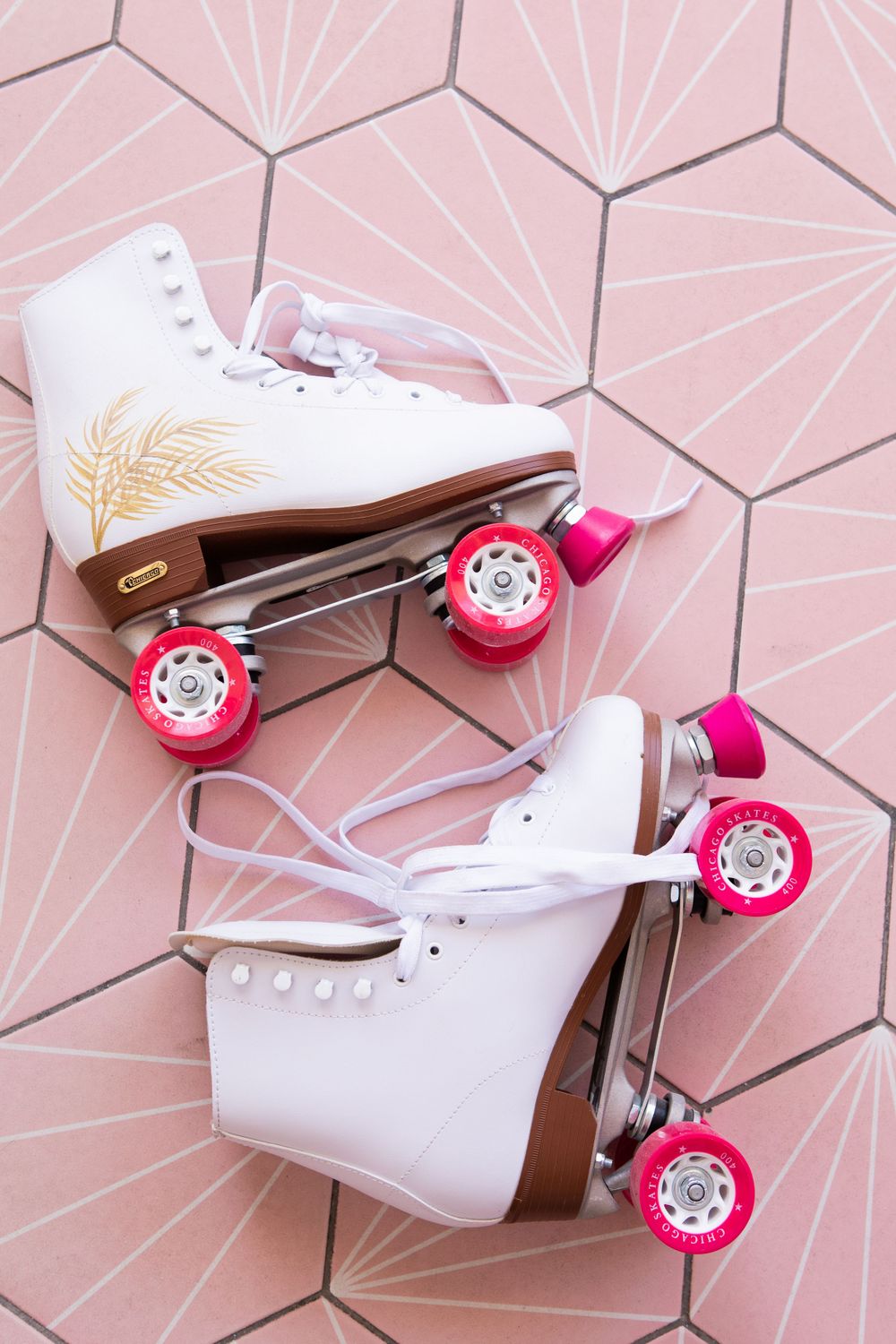 White vintage roller skates with pink wheels displayed on pink geometric tile pattern.