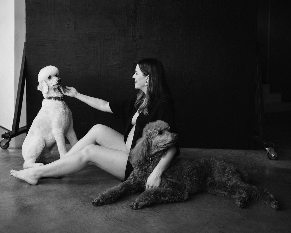 Black and white photo with person sitting between two dogs on concrete floor.