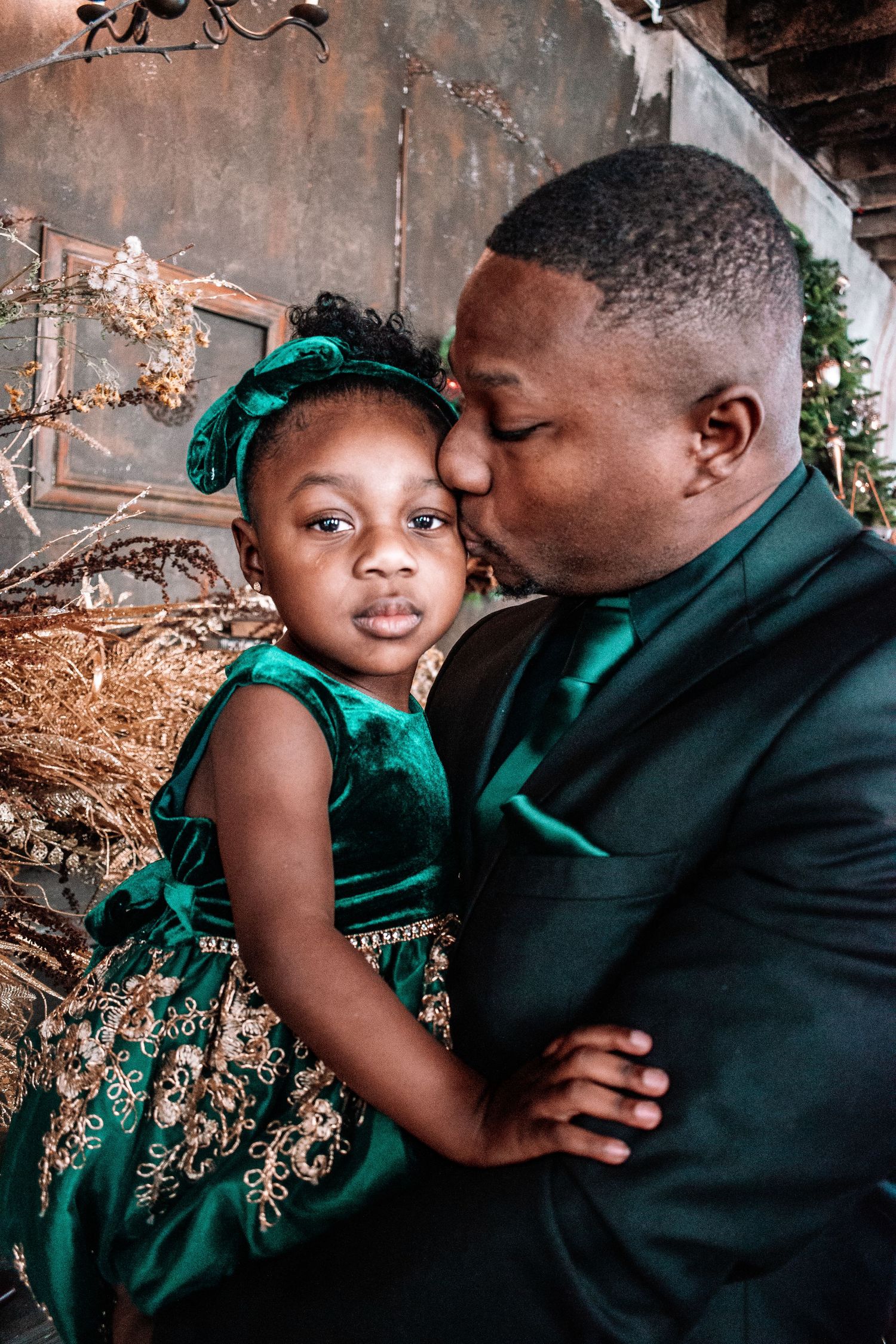Father and daughter. An elegant portrait featuring matching emerald green velvet formal wear against a rustic backdrop with twinkling lights