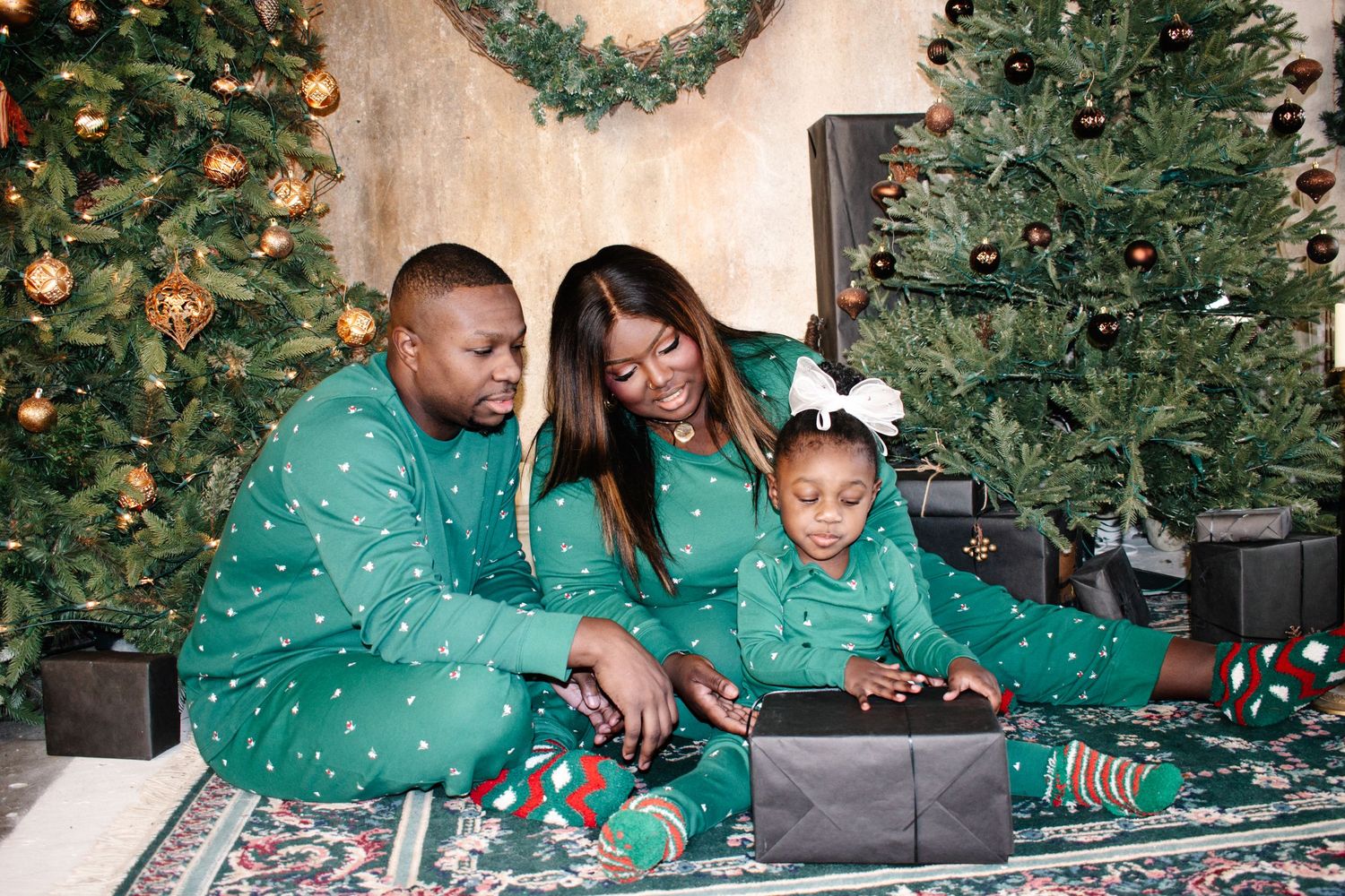 Tacoma family photography. Family wearing matching green pajamas sitting together on floor by Christmas trees with holiday decorations.