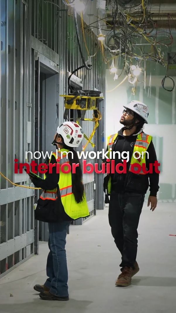 Two construction workers in hard hats and safety vests inspect an interior build-out at a commercial construction site.