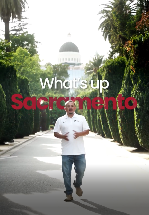 Man walking toward camera on tree-lined path with Sacramento Capitol dome backdrop and What's up Sacramento text overlay.