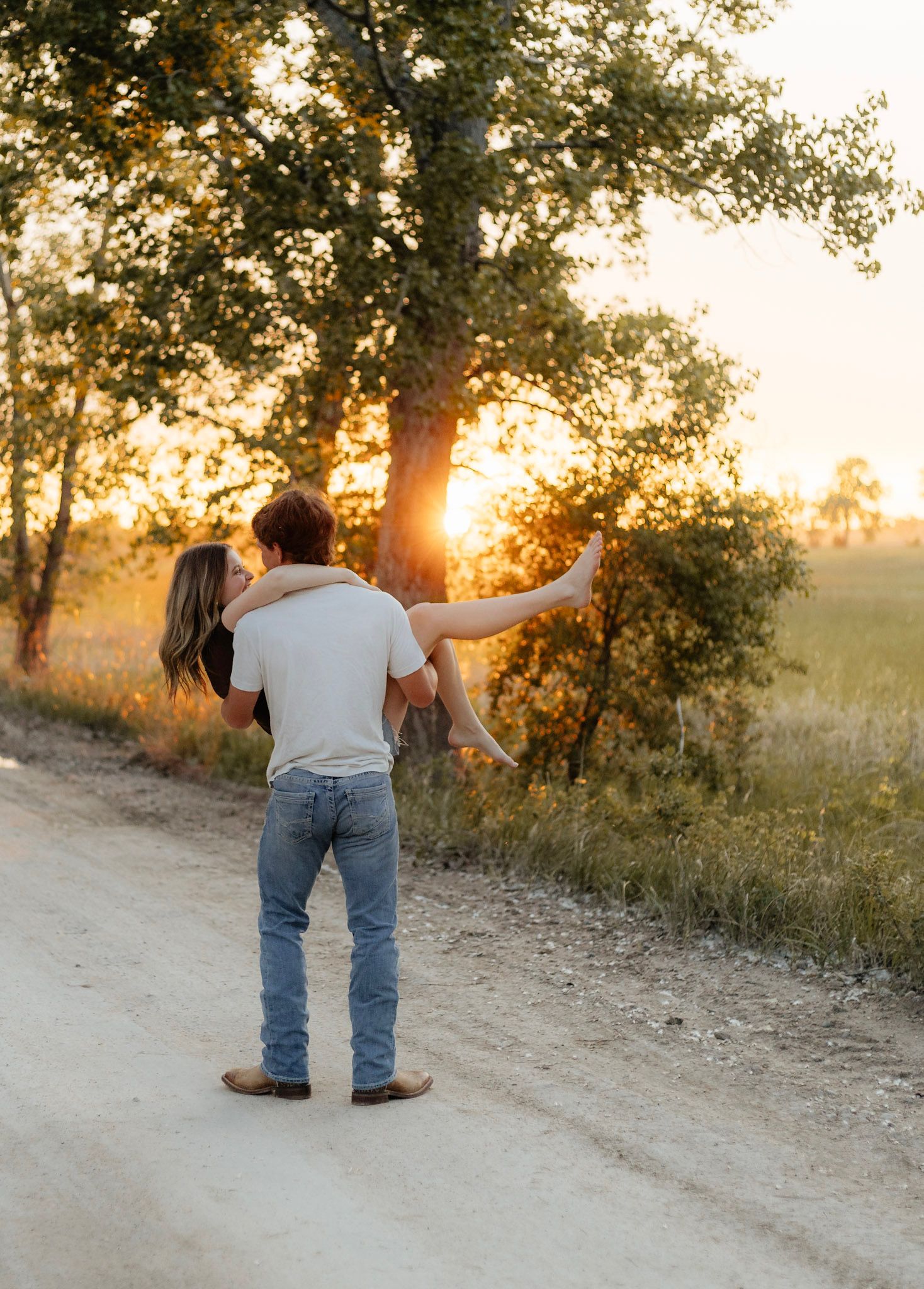 Two people walking along a dirt path during sunset with trees in background.
