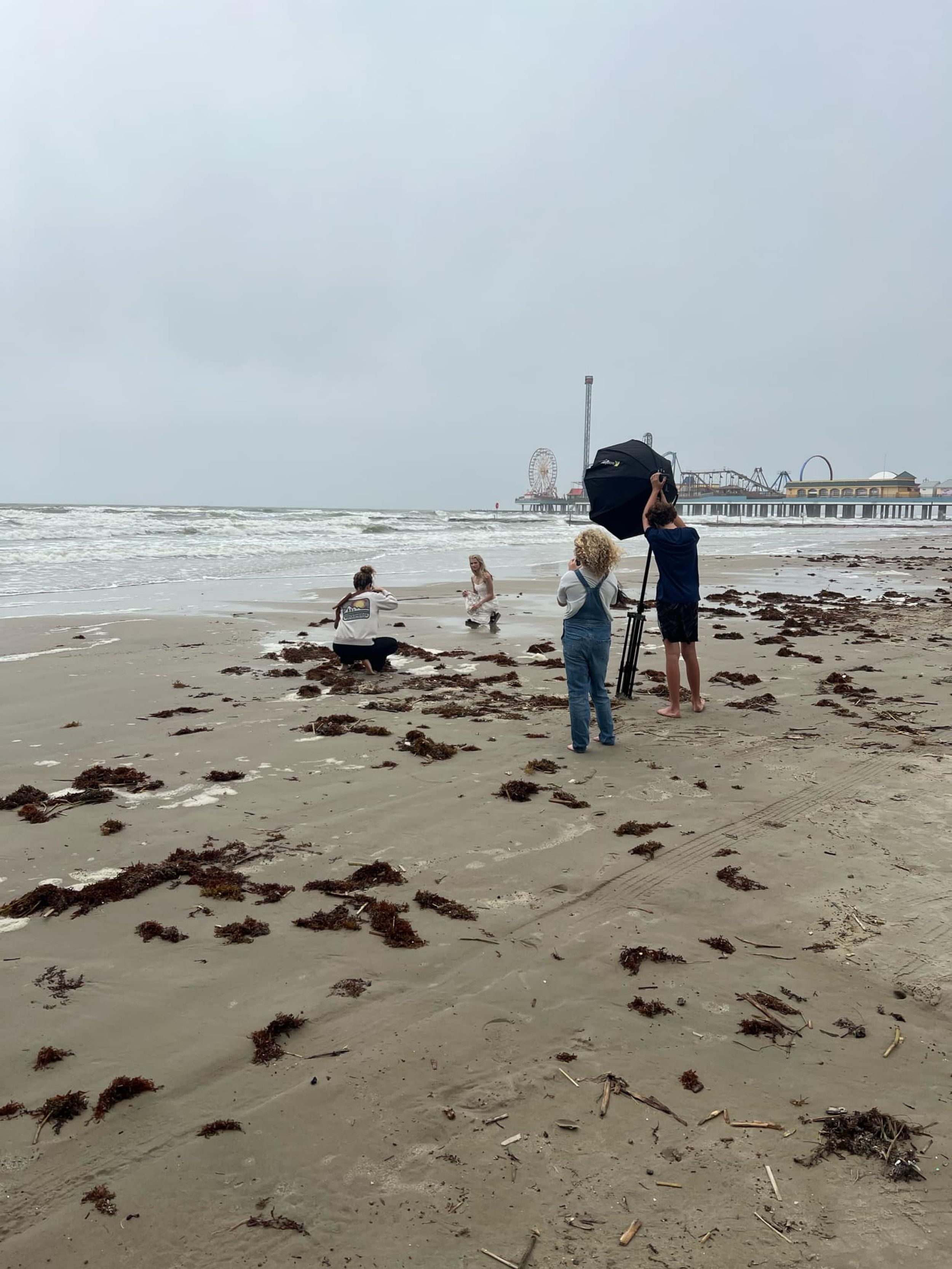 People enjoying a cloudy day at the beach with Pleasure Pier visible in the background at Galveston, Texas.