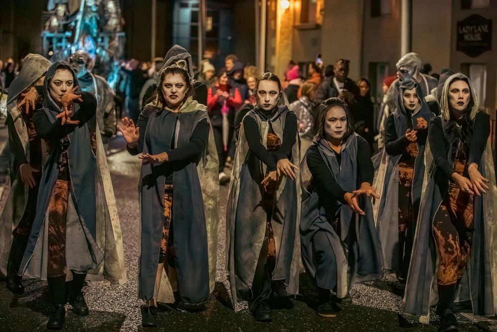 Medieval performers in period costumes walk through cobblestone streets during a historical reenactment festival.