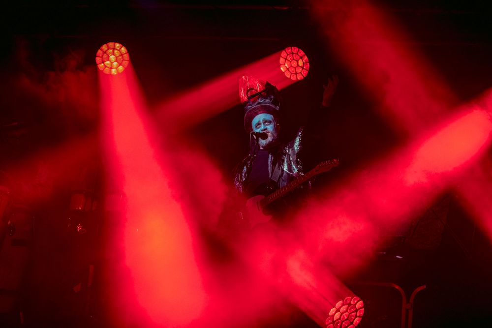 Red LED stage lights create dramatic beams through atmospheric haze during a concert performance.