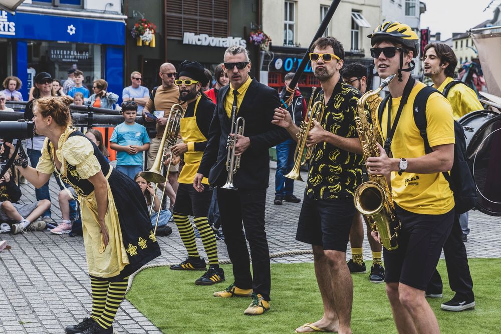 Street musicians with saxophones and instruments perform outdoors during a festival in casual summer attire.