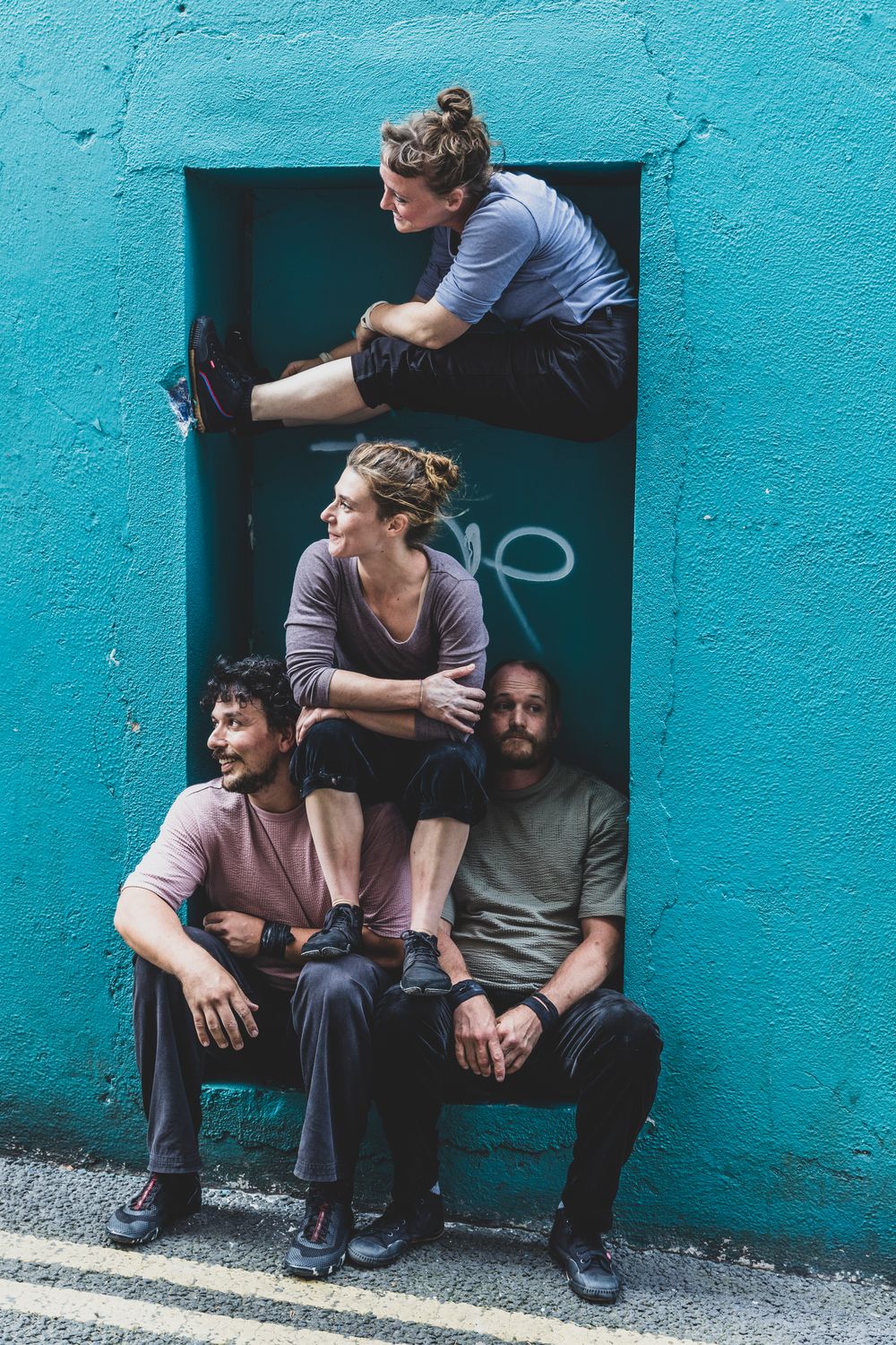Group sits casually against vibrant turquoise wall in urban setting creating artistic portrait series.
