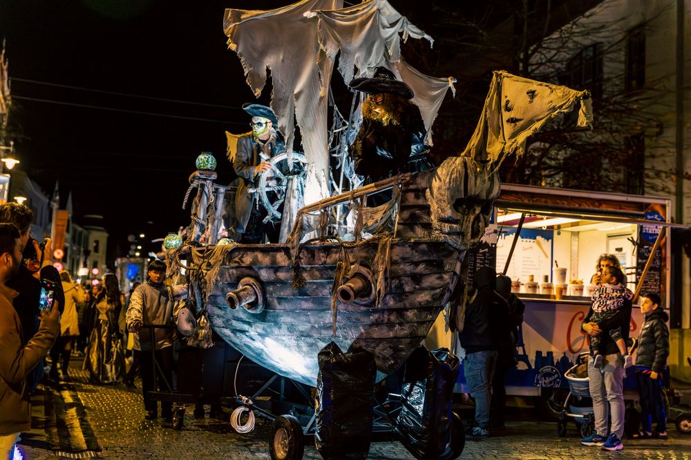 Nighttime street festival with illuminated stalls and crowds browsing vendors under warm lighting.