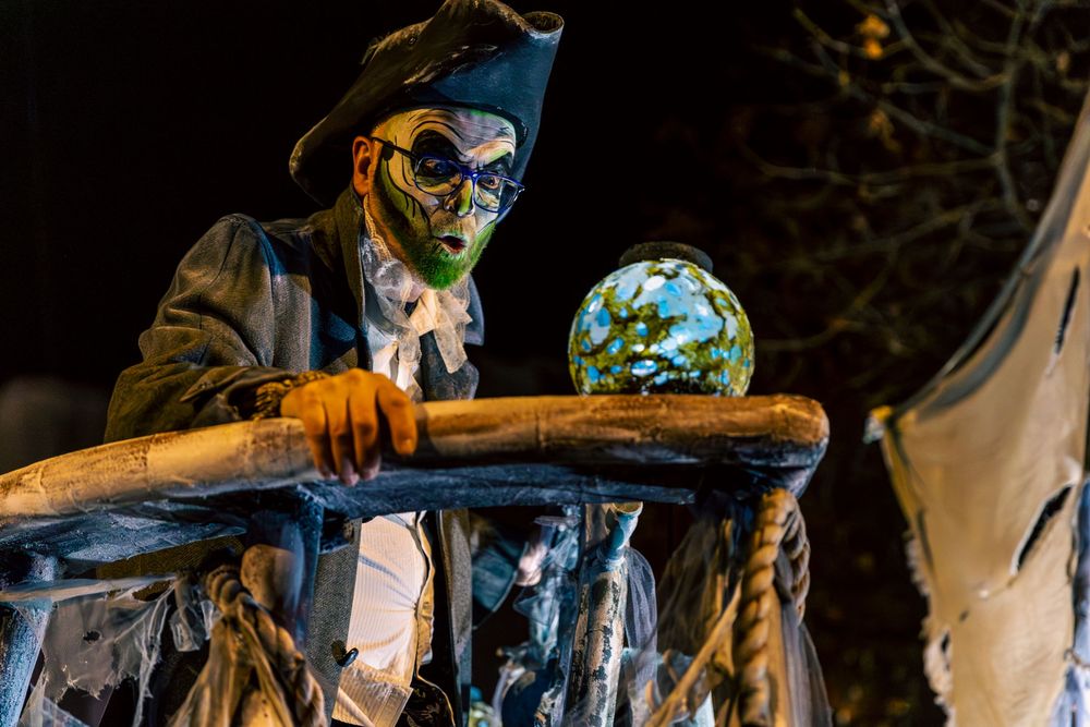 Medieval-themed performers in dark costumes gather at a nighttime festival with dramatic lighting.