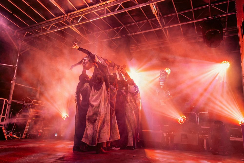 Theatrical performance with red smoke effects and dramatic backlighting on an outdoor stage.