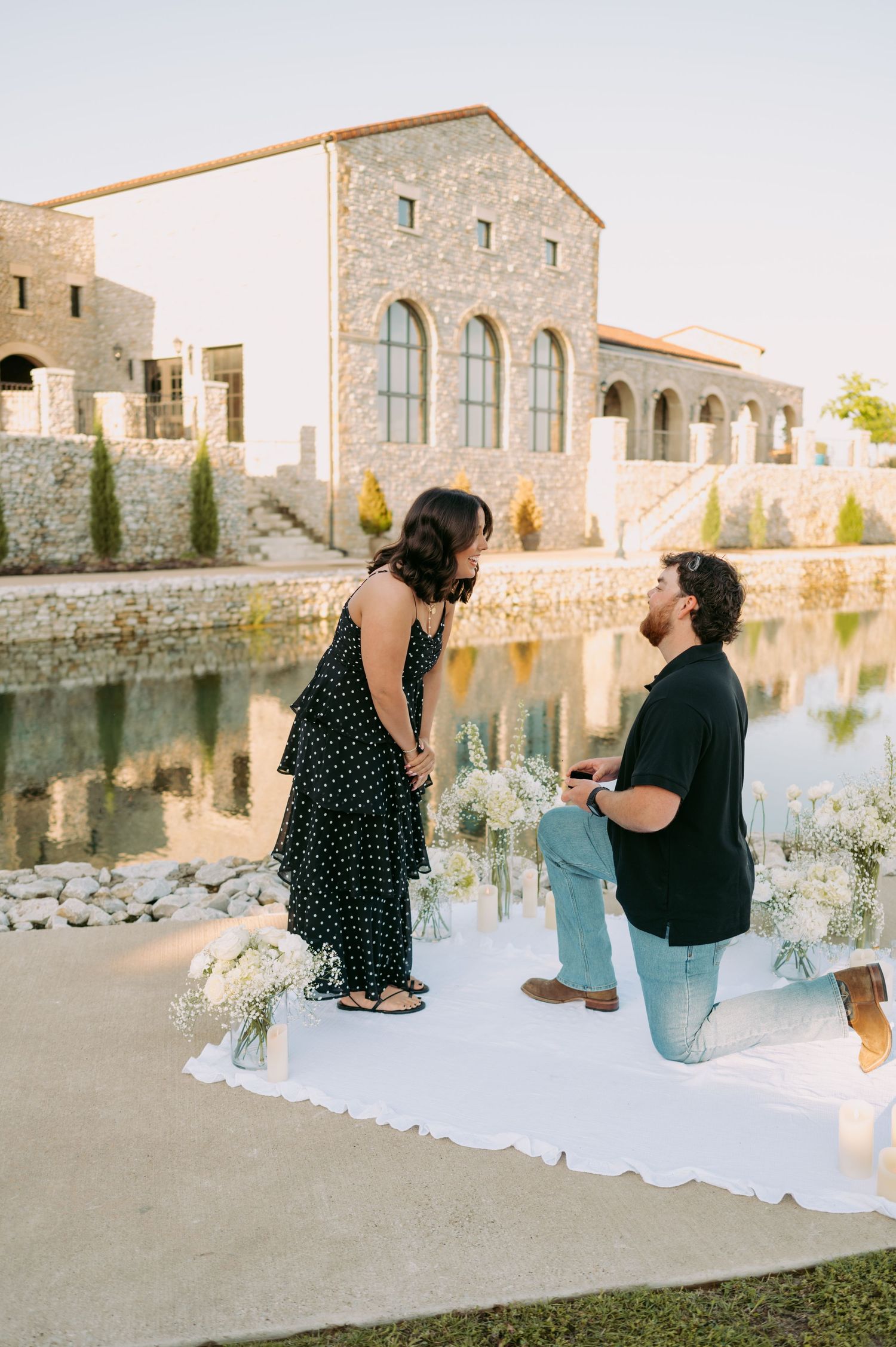 A surprise proposal setup with white decor near a stone building by the water.